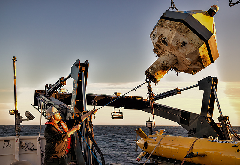 James Scott, an able seaman on NOAA Ship Okeanos Explorer, guides a NOAA buoy safely to the deck of the ship. This Pacific Marine Environmental Laboratory buoy had broken loose from its mooring and had been drifting around the Pacific — from California to Hawai‘i and back to California — for approximately two years before being recovered during the 2023 EXPRESS: Exploration of Central California Coast expedition.
