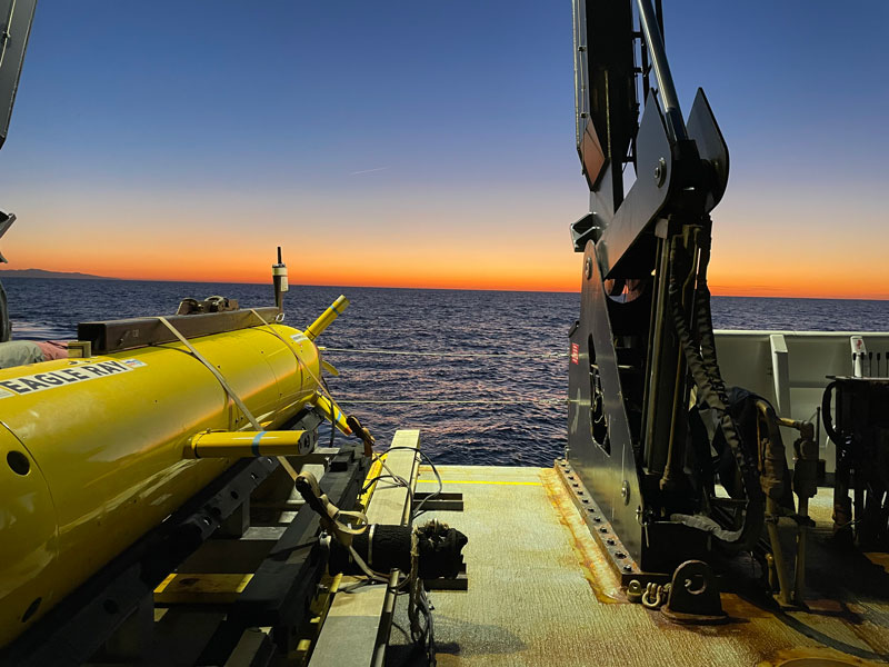 The sun sets over the back bow of NOAA Ship Okeanos Explorer and autonomous underwater vehicle Eagle Ray during the 2023 EXPRESS: West Coast Exploration (AUV and Mapping) expedition.
