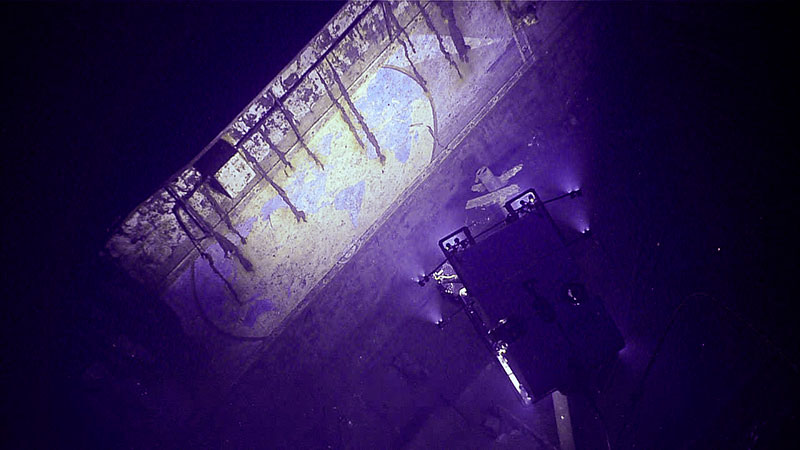 Underwater mural on shipwreck illuminated by purple lights with an ROV visible.