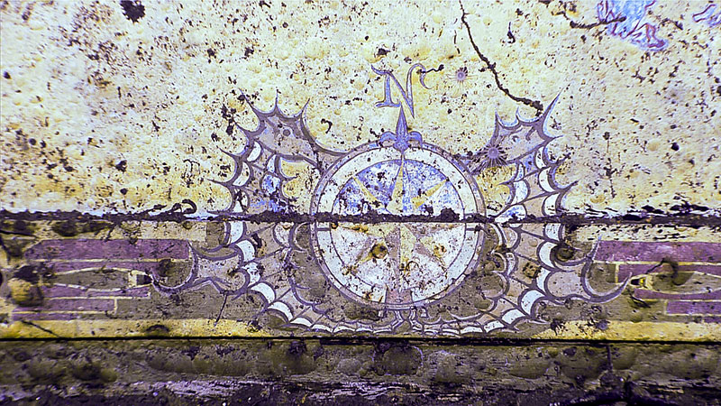 A faded mural of a compass rose with ornate wings on a weathered surface.