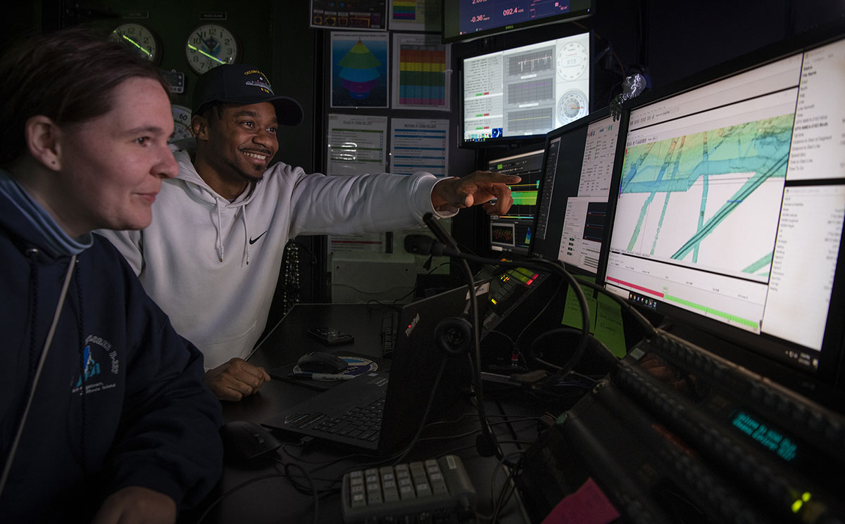 Explorers-in-Training Kathrin Bayer and Daryin Medley process mapping data in the control room aboard NOAA Ship Okeanos Explorer. Image courtesy Caitlin Bailey, GFOE.