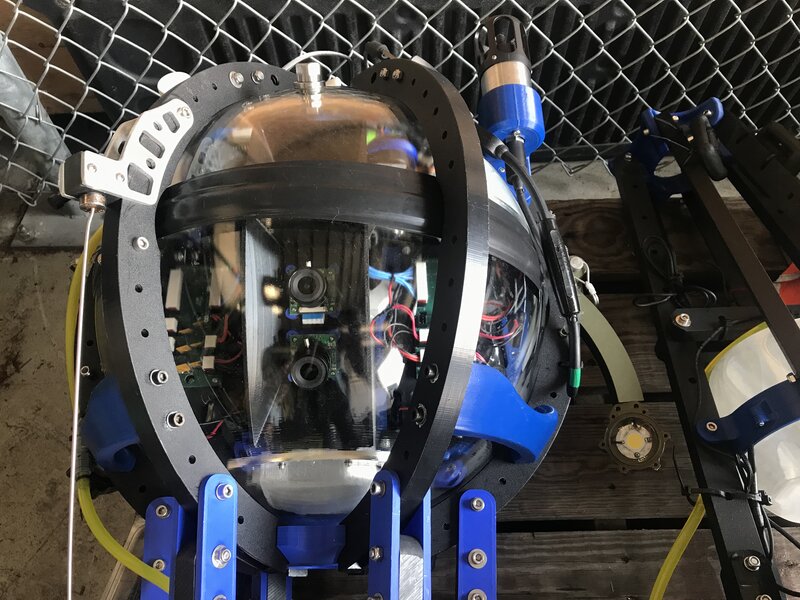 A closeup of the cameras enclosed within the glass sphere of the Driftcam. To the right of the sphere is one of the LEDs that provides lighting to the video cameras in the depths of the mid-ocean.