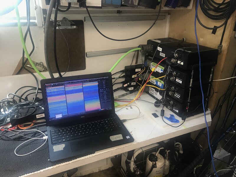 This laptop, showing three echograms, is hooked up to the four transceivers (black boxes on the right hand side of the photo). Each transceiver is hooked up to its respective transducer, which is housed in the transducer pod pole-mounted to the ship. Together, the transceivers and transducers make up the echosounder.